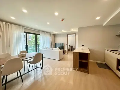 Modern open-plan living room with dining area and kitchen, featuring large windows and stylish decor.