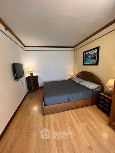 Cozy bedroom with wooden flooring, elegant bed, and wall-mounted TV, perfect for relaxation.