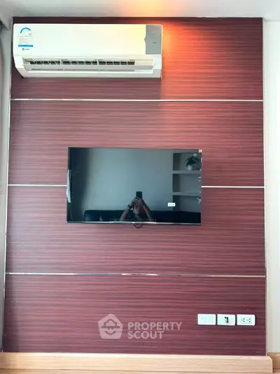 Modern living room with wall-mounted TV and air conditioning unit, featuring sleek wood paneling.