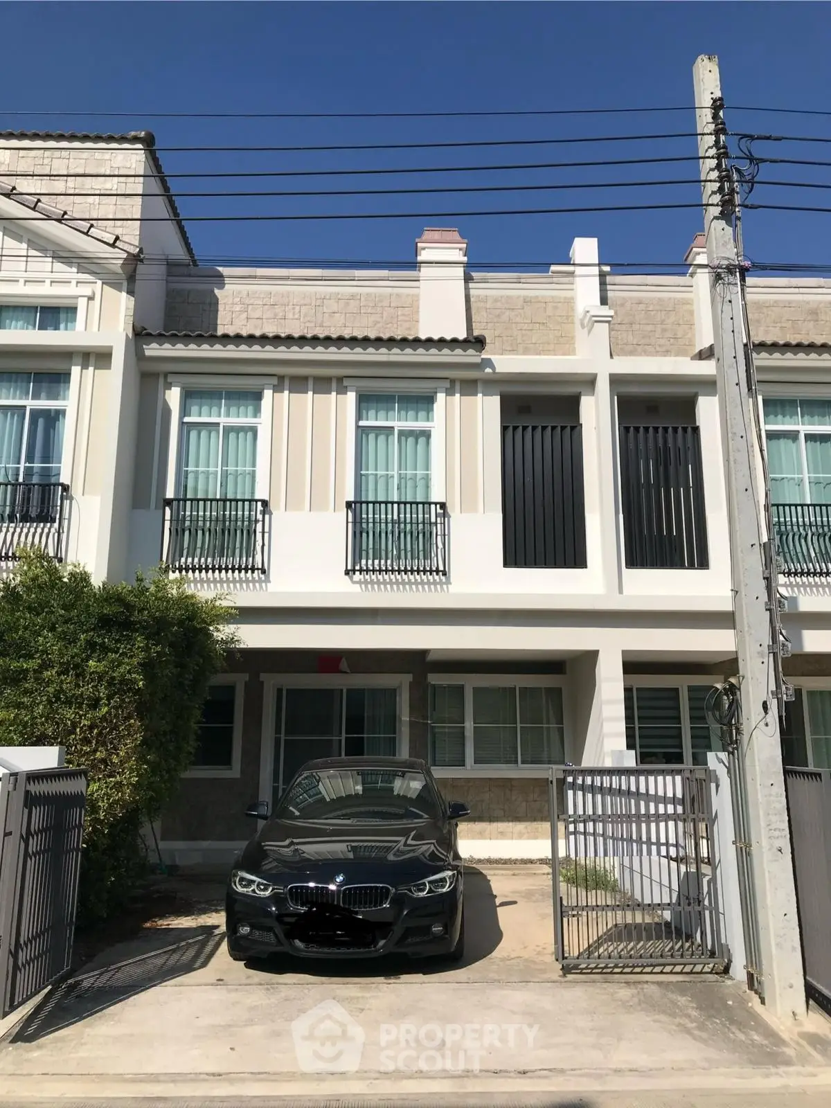 Modern townhouse exterior with driveway and parked car under clear blue sky.