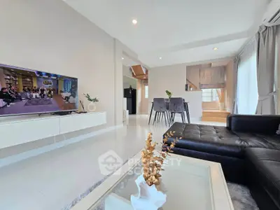 Spacious modern living room with sleek black sofa and wall-mounted TV, open dining area with natural light.