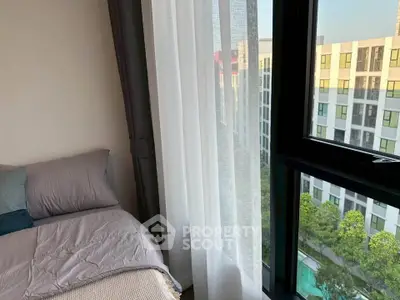 Cozy bedroom with large window offering a stunning view of modern building and pool area.