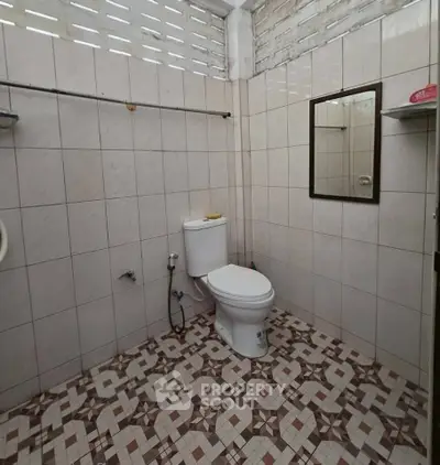 Spacious bathroom with tiled walls and floor, featuring a modern toilet and mirror.
