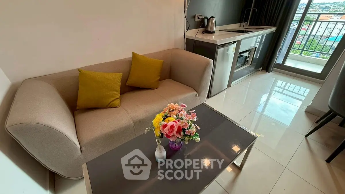 Modern living room with cozy sofa, sleek kitchenette, and vibrant city view from balcony.
