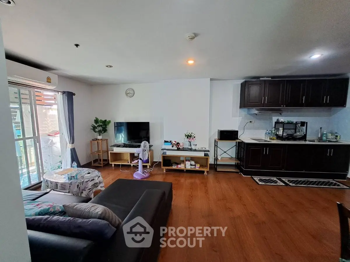 Spacious living room with modern kitchen, hardwood floors, and natural light from balcony.