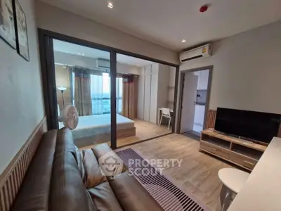 Modern open-plan living room with leather sofa and glass partition to bedroom, featuring stylish decor.