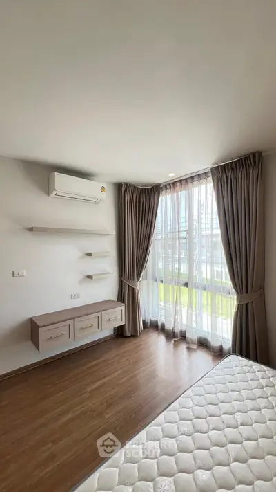 Spacious bedroom with large window and modern air conditioning unit, featuring elegant curtains and wooden flooring.