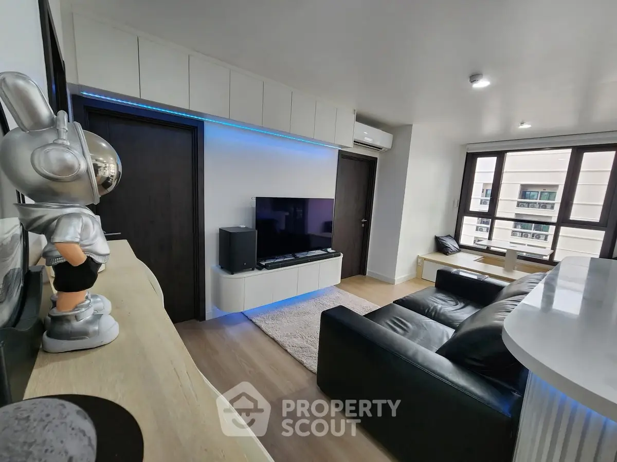 Modern living room with sleek black sofa and entertainment center, featuring stylish decor and large windows.