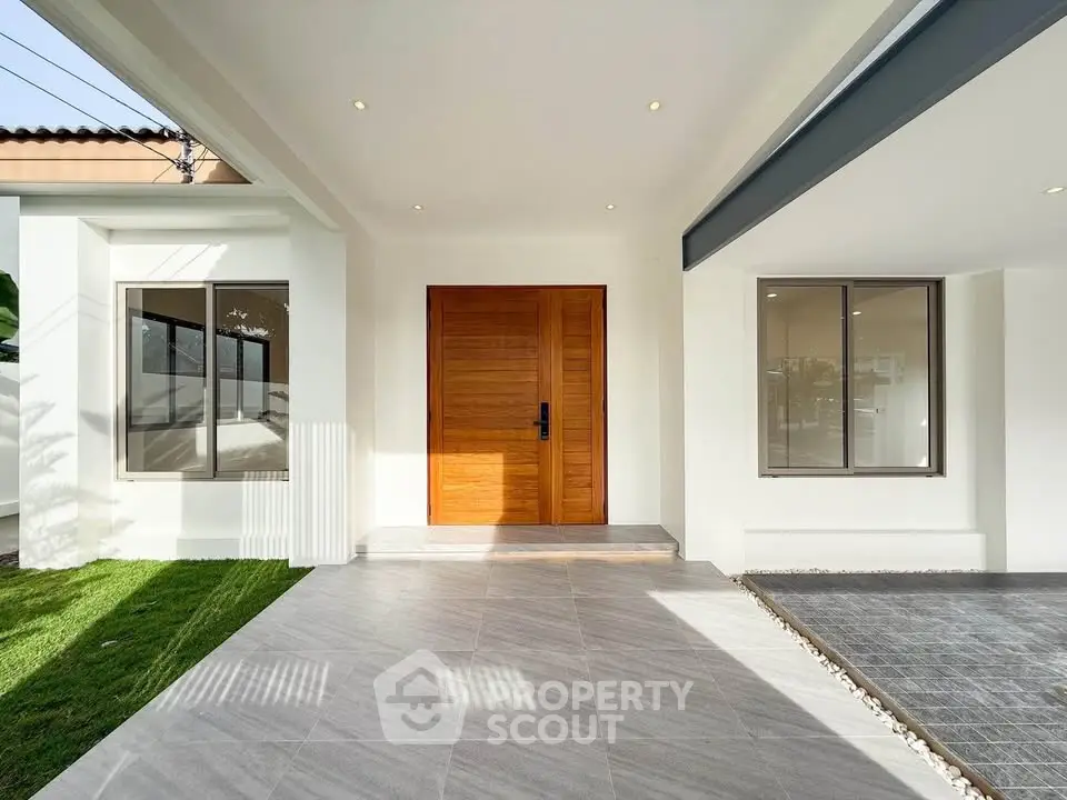 Modern home entrance with wooden door and sleek design, featuring a spacious patio and lush green lawn.