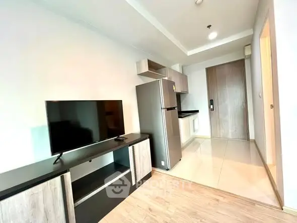 Modern apartment interior with sleek kitchen and living area featuring TV and fridge.