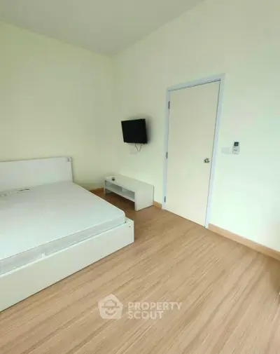Minimalist bedroom with wooden flooring and wall-mounted TV in modern apartment.