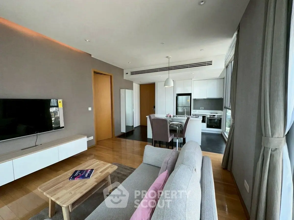 Modern open-plan living room with kitchen, featuring sleek furniture and large windows for natural light.