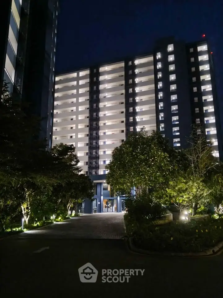 Stunning night view of a modern high-rise residential building with illuminated balconies and lush greenery.