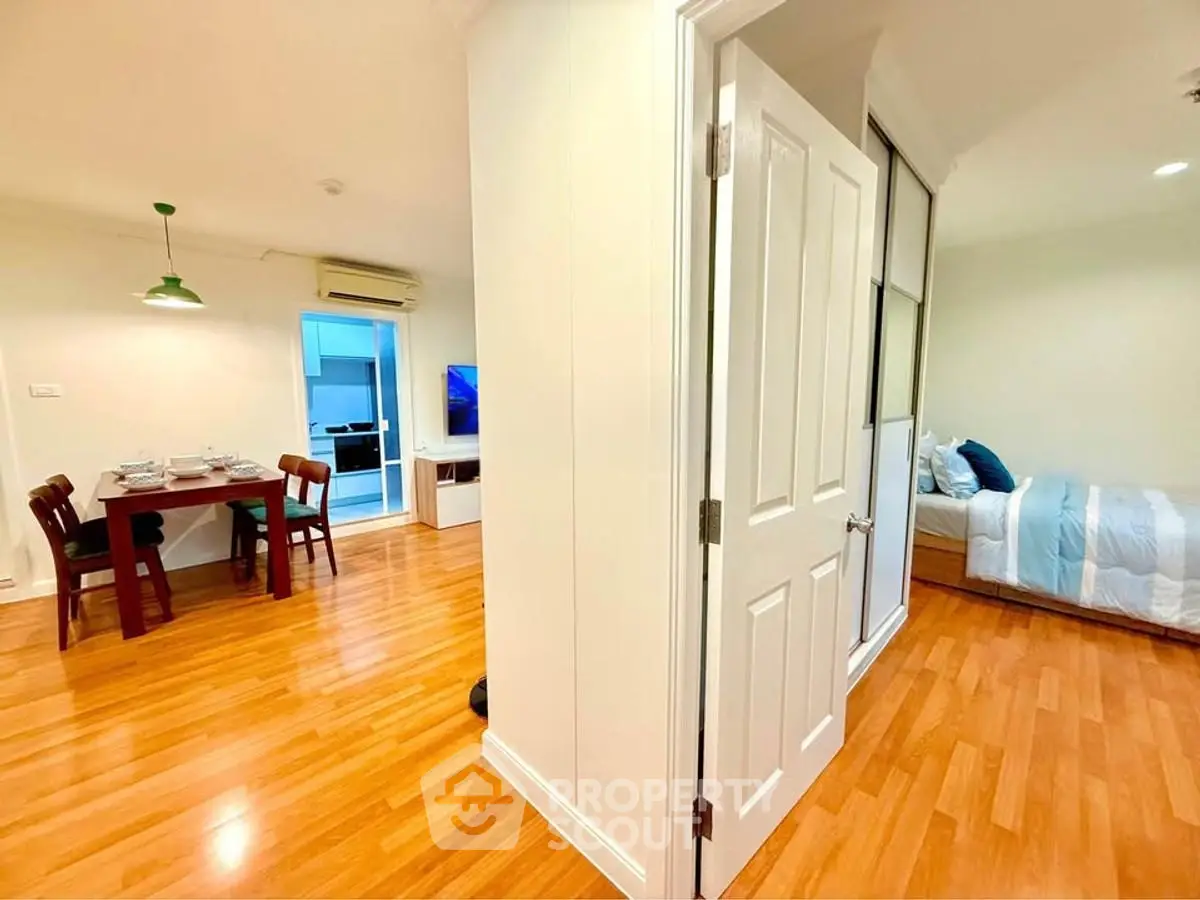 Spacious apartment with open dining area and cozy bedroom, featuring warm wooden flooring.