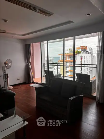 Spacious living room with large windows and balcony offering stunning city views.