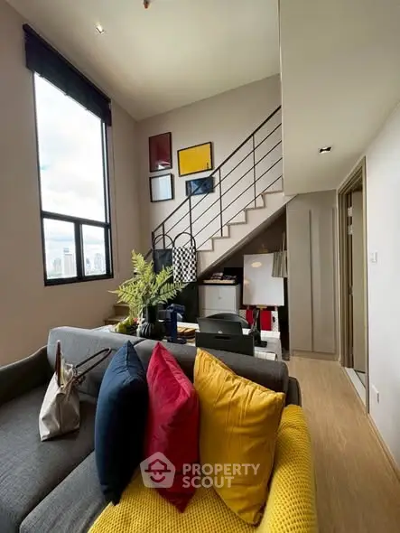Stylish modern living room with high ceiling and staircase, vibrant decor, and large window view.