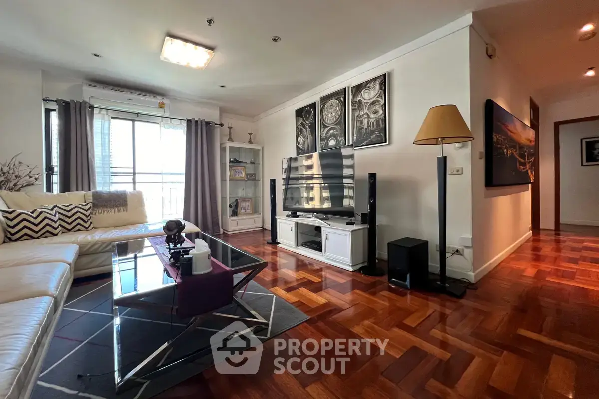Spacious living room with modern decor and large TV, featuring elegant wooden flooring.
