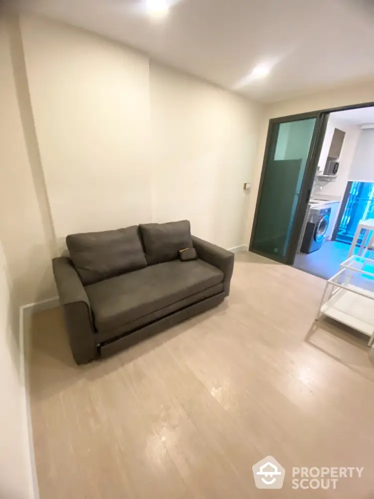 Modern living room with cozy sofa and sliding glass door leading to kitchen area.