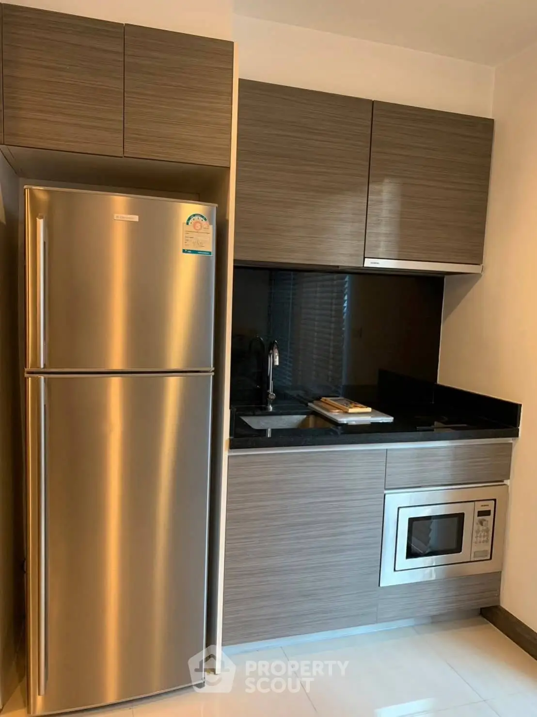Modern kitchen with sleek cabinetry, stainless steel fridge, and built-in microwave in a compact layout.