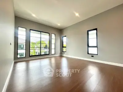 Spacious empty room with large windows and wooden flooring, perfect for customization.