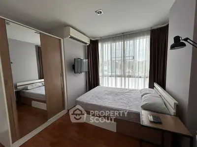 Cozy bedroom with large window, mirrored closet, and wall-mounted TV in modern apartment.