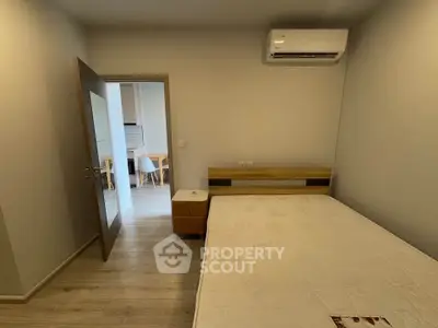 Modern bedroom with air conditioning and wooden flooring, leading to a bright kitchen area.