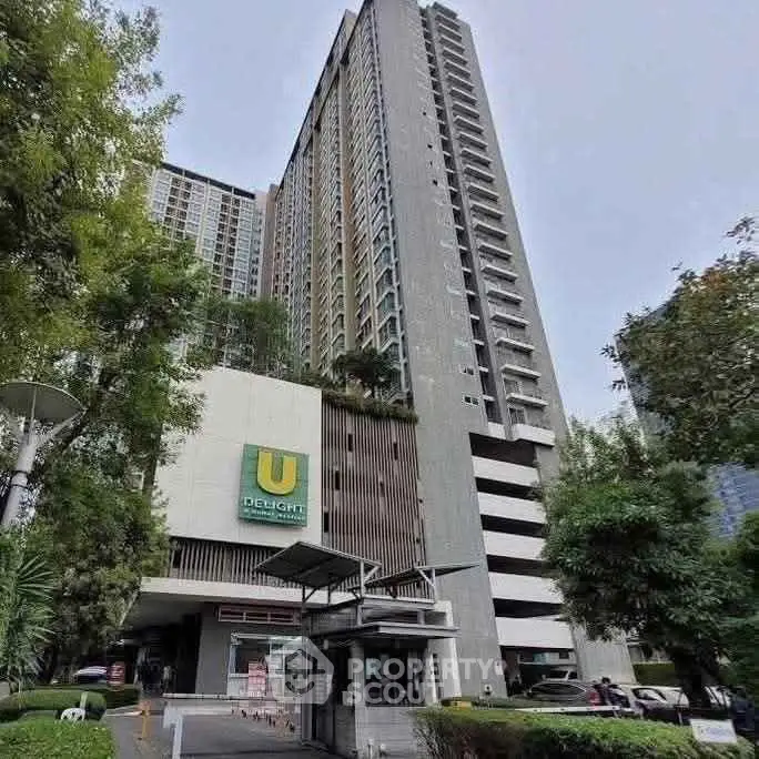 Modern high-rise condominium with lush greenery and sleek architecture in urban setting.