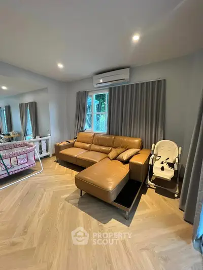 Spacious living room with modern leather sofa and baby furniture, featuring elegant wooden flooring.