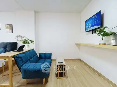 Modern living room with blue sofa, wall-mounted TV, and wooden flooring