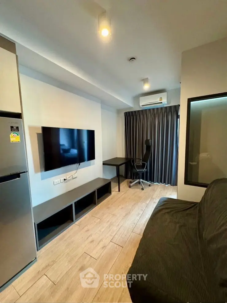 Modern living room with TV, fridge, and study area in stylish apartment.