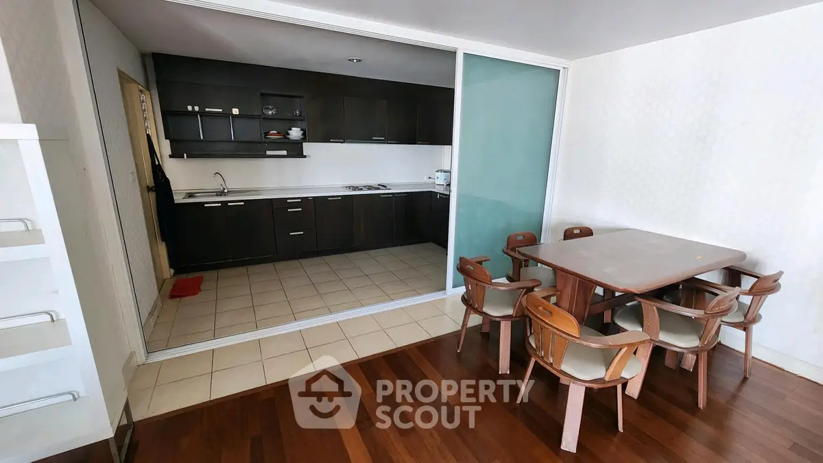 Modern kitchen with dark cabinets and dining area with wooden table and chairs.
