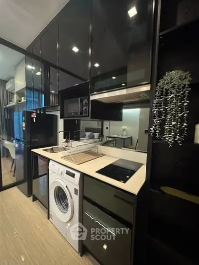 Modern kitchen with sleek black cabinets, built-in appliances, and washing machine in compact layout.