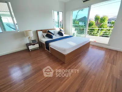 Spacious bedroom with large windows and wooden flooring, offering a serene view.