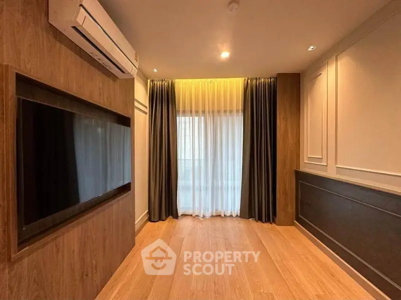 Modern living room with wooden flooring, large TV, and elegant curtains.