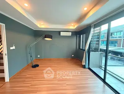 Spacious modern living room with wooden flooring and large windows leading to balcony.