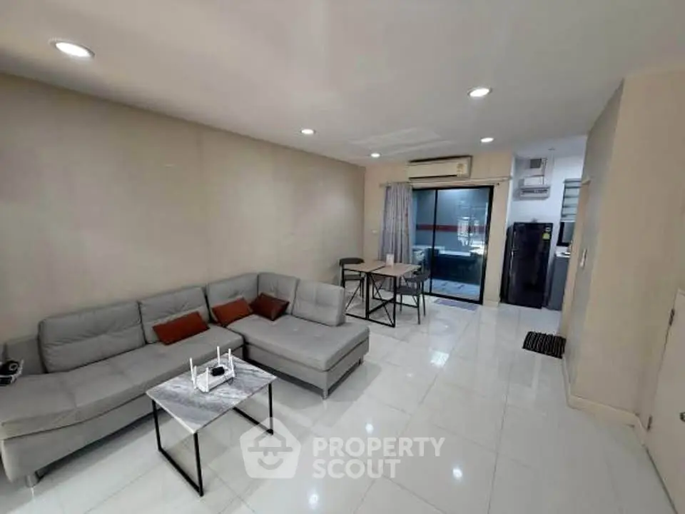 Modern living room with sleek gray sectional sofa and open layout leading to dining area and kitchen.