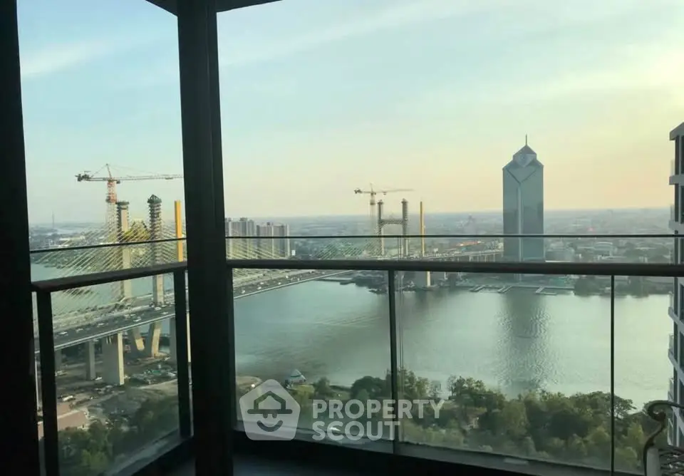 Stunning high-rise balcony view overlooking river and city skyline with cranes and bridge.