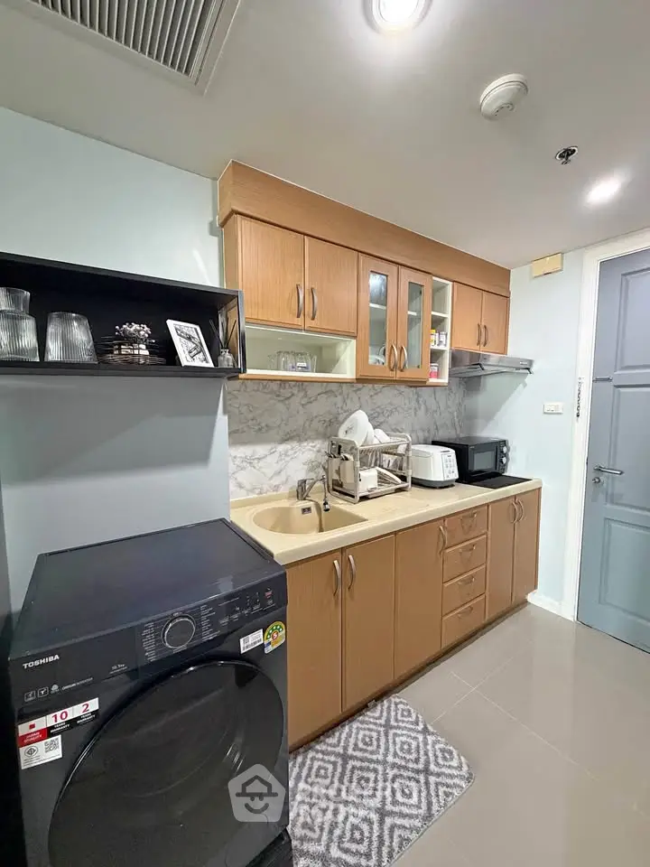 Modern kitchen with wooden cabinets, marble backsplash, and appliances including washing machine and microwave.