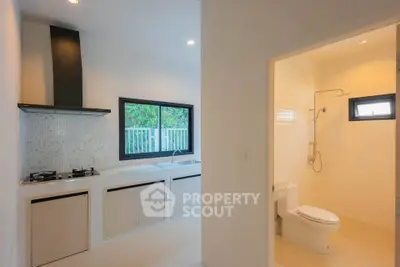 Modern kitchen with gas stove and adjacent bathroom in a bright, airy home.