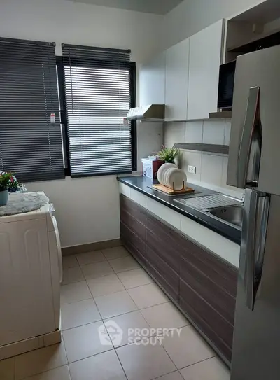 Modern kitchen with sleek cabinets and appliances, featuring a washing machine and large fridge.