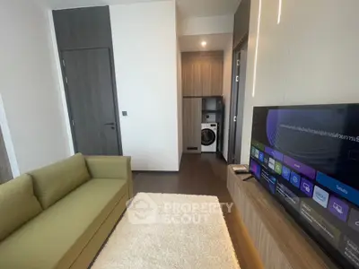 Modern living room with green sofa and TV, featuring a washing machine in the background.