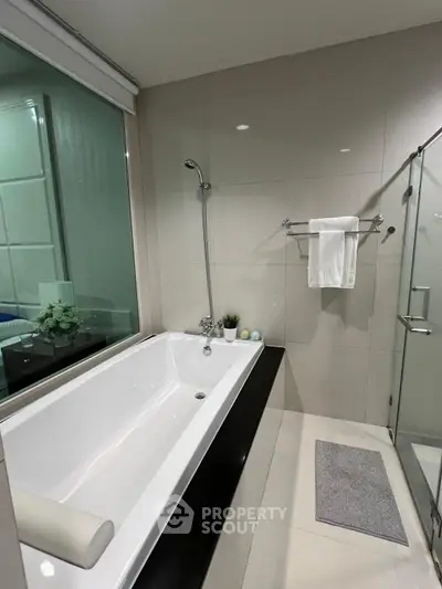 Modern bathroom with sleek bathtub and glass shower enclosure in a stylish apartment.