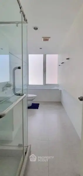 Modern bathroom with glass shower and large window, offering a sleek and minimalist design.