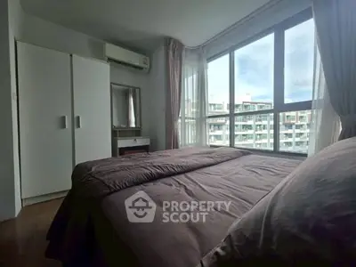 Cozy bedroom with large windows offering a stunning city view, featuring a wardrobe and air conditioning.