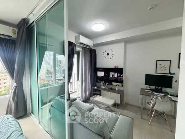 Modern living room with glass partition and city view, featuring cozy seating and a work desk.