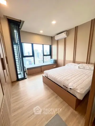 Modern bedroom with city view, featuring wooden flooring and built-in storage.
