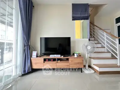 Modern living room with sleek TV console and staircase, featuring large windows and stylish curtains.