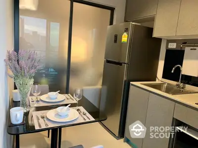 Modern compact kitchen with dining area, featuring sleek cabinets and stainless steel fridge.