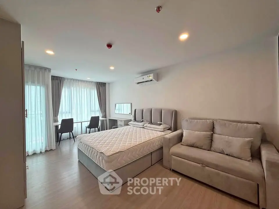 Spacious modern bedroom with cozy sofa and large window in a stylish apartment.