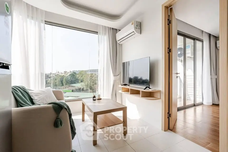 Bright modern living room with large windows and scenic view, featuring cozy seating and sleek TV setup.